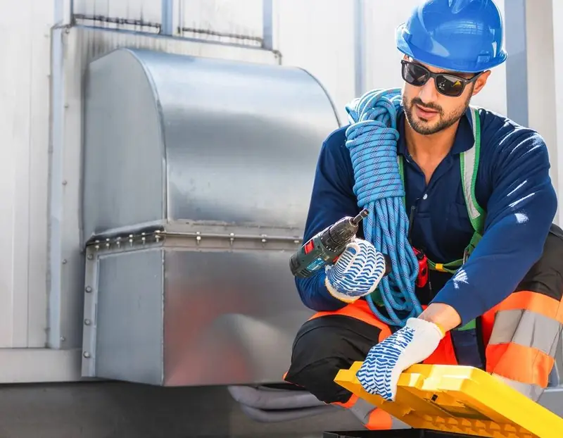 Technician in a hard hat beside galvanized ductwork